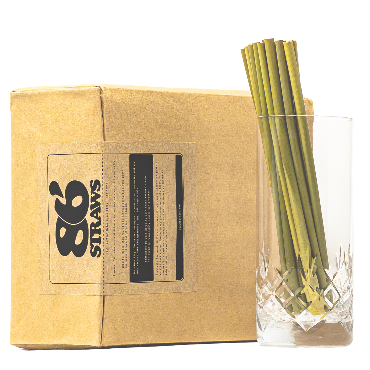 A kraft paper box with a black 86 Straws logo label sits next to a clear cut-glass tumbler holding several green straws, photographed on a white background.