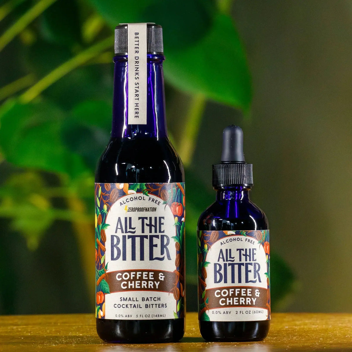 All The Bitter Coffee & Cherry alcohol-free cocktail bitters in 5 oz bottle and 2 oz dropper bottle against green foliage