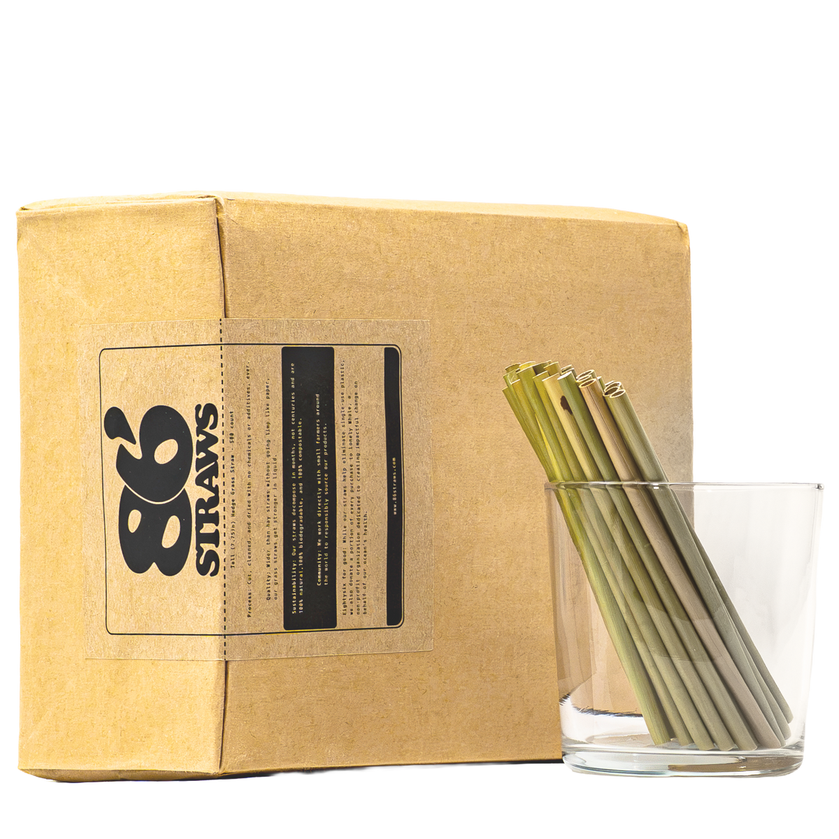 A kraft paper box with a clear window showing green and beige reusable drinking straws inside, alongside a clear glass holding several of the straws. The box label reads '86 STRAWS'.