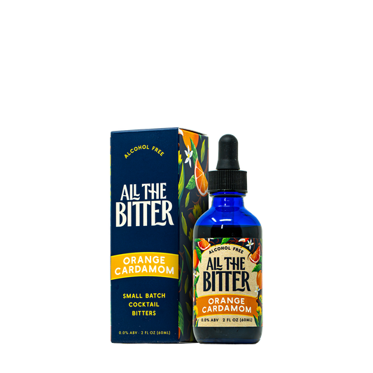 A bottle of All The Bitter Alcohol Free Orange Cardamom tincture next to its dark blue packaging box, featuring a blue cobalt glass bottle with a black dropper cap and a label decorated with orange slices.