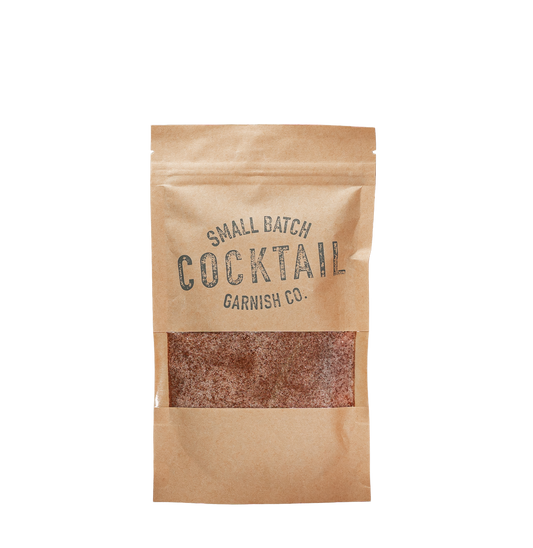 A small kraft paper resealable pouch with a clear window showing a brown textured product inside. The pouch has dark printed text reading 'SMALL BATCH COCKTAIL GARNISH CO.