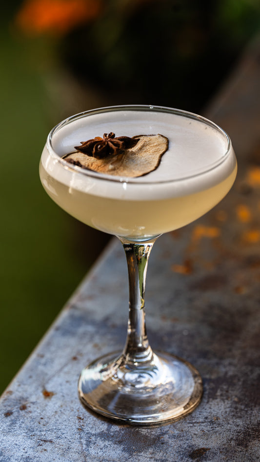 Dried Pear Garnishes floating on top of a cocktail in a coupe glass with a foam head and star anise floating