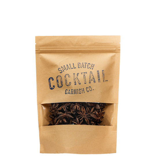 A small kraft paper stand-up pouch with a clear window showing dried star anise inside. The pouch is printed with the text 'SMALL BATCH COCKTAIL GARNISH CO.