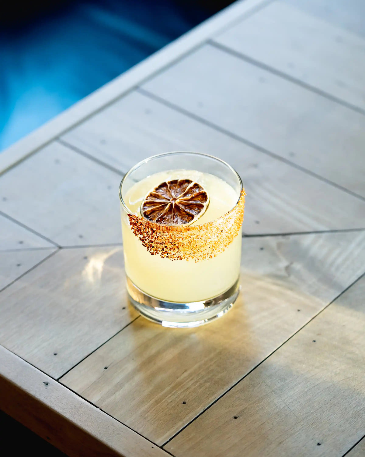 Dehydrated lime wheel on a rocks glass margarita with a chili-lime rimmed edge, on a sunlit wooden table
