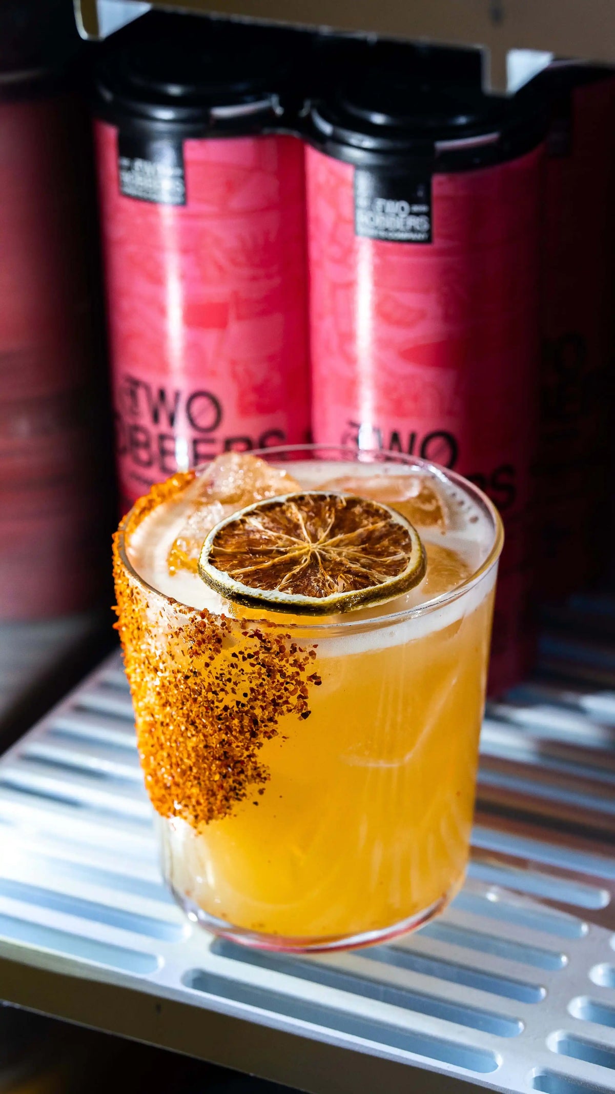 Dehydrated lime wheel on a rocks glass with a red chili-lime rimmed edge, filled with an orange cocktail over ice